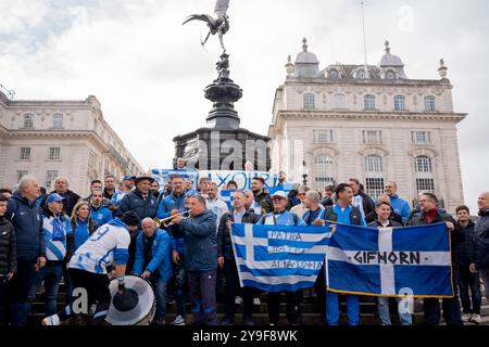 Stunden vor dem Spiel der UEFA Nations League gegen England in Wembley versammeln sich griechische Fußballfans, um am 10. Oktober 2024 im Piccadilly Circus in London unter der Skulptur Eros zu singen. Stockfoto