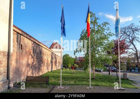 TARGU MURES, RUMÄNIEN - 5. MAI 2023: Dies sind Fahnenmasten mit den Flaggen der Europäischen Union, Rumäniens und der Stadt in der Nähe der Mauern der mittelalterlichen Festung Stockfoto