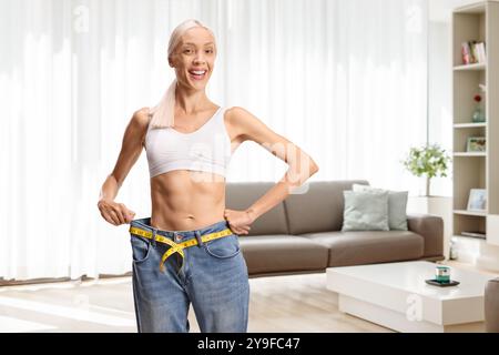 Eine Frau mit Happy Fit-Effekt in alten Jeans und Crop-Top-Maßen-Abfall mit Klebeband zu Hause Stockfoto