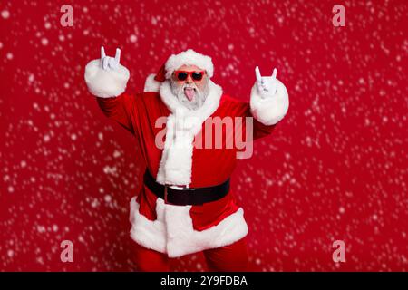 Portrait von attraktiven verrückt fröhlich kindisch Santa zeigt Horn Symbol mit Spaß isoliert über hellen roten Hintergrund Stockfoto
