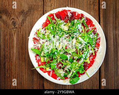 Ein Teller mit dünn geschnittenem Carpaccio, belegt mit frischen Rucolablättern und Parmesanspänen. Stockfoto