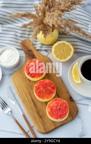 Blick von oben auf frische Mini-Obst-Crumble-Käsekuchen auf einem Holzbrett mit Kaffee, Zitrone und einer dekorativen Vase. Stockfoto