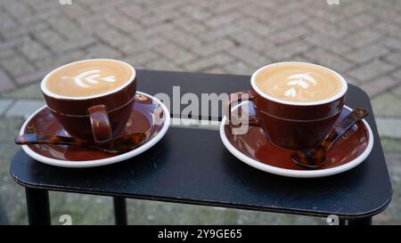 Zwei flache weiße Kaffeetassen mit Blumenschaum Latte Art auf Untertassen auf einem Tisch. Barista-Kaffee im Café-Stil. Stockfoto
