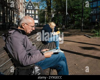 Menschen sitzen auf Bänken, lesen Bücher und entspannen sich an einem seltenen sonnigen Tag in Amsterdam. Stockfoto