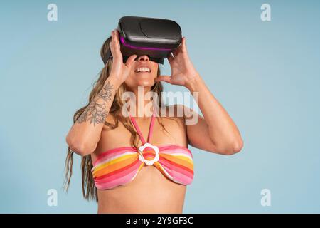 Porträt einer schönen brünetten lateinamerikanischen Frau mit langen Haaren, die eine Virtual-Reality-Brille mit lustiger Attitüde trägt und einen rot-gelb gestreiften Bikini aga trägt Stockfoto