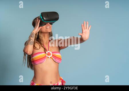 Porträt einer schönen brünetten lateinamerikanischen Frau mit langen Haaren, die eine Virtual-Reality-Brille mit lustiger Attitüde trägt und einen rot-gelb gestreiften Bikini aga trägt Stockfoto