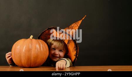 Halloween-Kind im Hexenhut mit Halloween-Kürbis. Frohe Halloween-Feiertage. Lächelnder Junge im Halloween-Kostüm mit Jack-o-Laternenkürbis. Danke Stockfoto