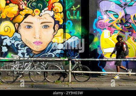 Ein Mann mit Kopfhörern spaziert entlang einer bunten Wall Street Art Berlin Deutschland Stockfoto