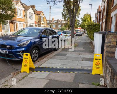 Kia Elektroauto lädt in einer Wohnstraße vom Haus aus mit Straßenschutzkabeln für das EV-Ladekabel auf, London, Großbritannien Stockfoto