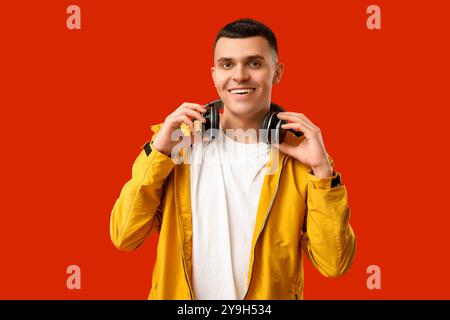 Junger Mann in stilvoller Jacke und Kopfhörern auf rotem Hintergrund Stockfoto