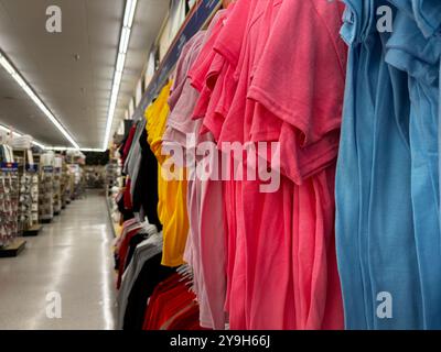 Eine Ausstellung farbenfroher gefalteter T-Shirts auf Kleiderbügeln in einem gut beleuchteten Gang Stockfoto