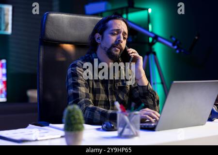 Männlicher Freelancer, der moderne Kommunikationstechnologie nutzt, während er im Internet surft. Bärtiger Mann, der telefoniert und auf seinem Laptop schreibt. Stockfoto