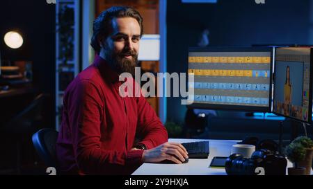 Glücklicher Fotograf, der Bilder auf Computermonitoren bearbeitet. Porträt eines lächelnden Fotoredakteurs, der Farbabstufungen auf Fotos im Büro eines kreativen Studios durchführt Stockfoto