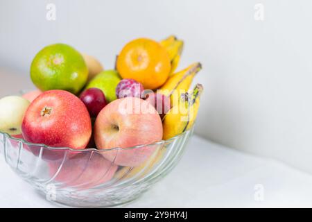 Eine Glasschale gefüllt mit einer Vielzahl von frischen Früchten einschließlich Äpfeln, Bananen, Orangen und Trauben. Die Früchte sind bunt und attraktiv angeordnet. Stockfoto