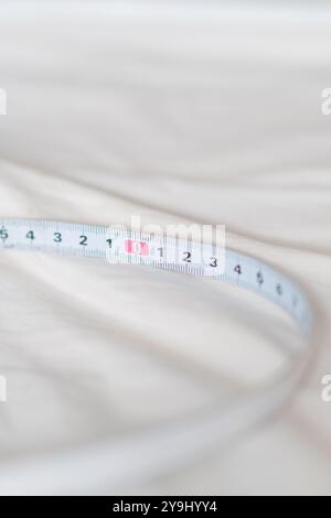 Nahaufnahme eines Maßbandes auf einer weichen, hellen Oberfläche. Das Band zeigt Zahlen deutlich, wobei der Fokus auf der Nullmarke liegt, was p angibt Stockfoto