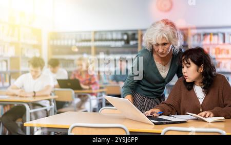 Ältere Lehrerin hilft Schülerinnen, die Gleichung in der Schulbibliothek zu lösen Stockfoto