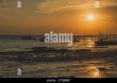 Ein atemberaubender Sonnenuntergang, der lange Schatten über das ruhige Wasser wirft. Die Boote schweben sanft vor Anker, während die Menschen entlang des Piers spazieren und den Frieden genießen Stockfoto