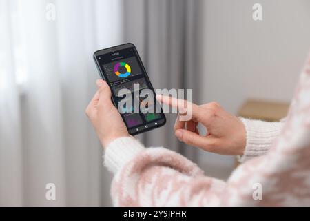 Frau überwacht intelligente Zählerstände auf dem Handy zu Hause, Nahaufnahme Stockfoto