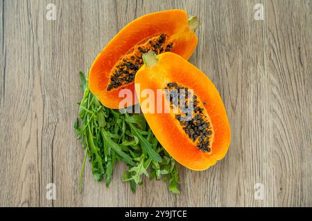 Papaya-Frucht und Rucola auf hellem Holzhintergrund. Scheiben süßer Papayas auf hölzernem Hintergrund, halbierte Papayas, Kopierraum für Text Stockfoto