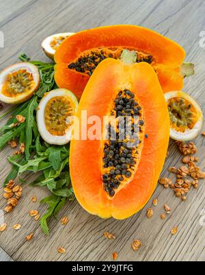 Papaya-Frucht, Passionsfrucht, Rucola und Müsli auf hellem hölzernem Hintergrund. Scheiben süßer Papaya, Maracuja, grüner Rucola umgeben von Granola fla Stockfoto