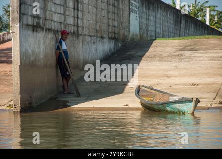 Tlacotalpan, Veracruz, Mexiko; 06 12 2012: Ein Mann, der sich an die Mauer neben dem Fluss lehnt und sein Boot. Stockfoto