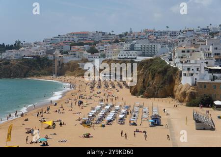 Lebhafter Sandstrand mit vielen Menschen und Liegestühlen vor malerischen Klippen und einer Küstenstadt, Albufeira, Faro, Algarve, Portugal, Europa Stockfoto