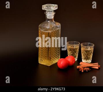 Pflaumenlikör mit Zimt und Anis, starker hausgemachter Alkohol in einer Kristallflasche und zwei Gläser auf schwarzem Hintergrund, neben Reifen Früchten. Nahaufnahme Stockfoto