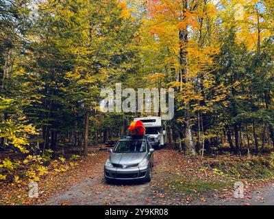 Campingplatz im Wald im Herbst - Auto und Wohnmobil unter den Bäumen. Kajaks auf dem Dach des Autos Stockfoto