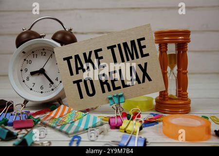 Nehmen Sie sich Zeit, um Text auf Papierkarte mit Wecker und stationärem Hintergrund auf hölzernem Hintergrund zu entspannen Stockfoto