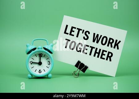 Arbeiten wir gemeinsam eine Textnachricht auf Papierkarte mit Wecker auf grünem Hintergrund Stockfoto