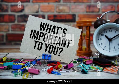 Was ist Ihnen wichtig? Text auf Papierkarte mit Wecker und stationär auf hölzernem Hintergrund Stockfoto
