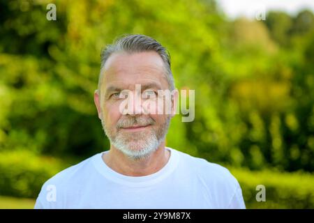 Ein Porträt eines Reifen Mannes mit grauem Haar und kurzem Bart, der draußen steht und der Kamera zugewandt ist. Stockfoto