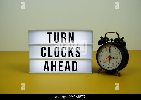 Drehen Sie die Uhr voran Text auf dem Leuchtkasten mit Wecker auf gelbem Hintergrund Stockfoto