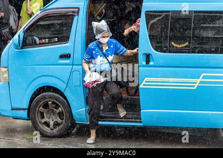 SAMUT PRAKAN, THAILAND, 04. Oktober 2024, Eine Frau steigt aus dem Minivan mit überdachtem Kopf einer Plastiktüte gegen Regen Stockfoto