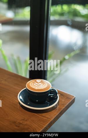 Porträt- oder vertikale Aufnahme einer Tasse Kaffee mit herzförmiger Latte Art auf einem Holztisch mit Bokeh-Hintergrund Stockfoto