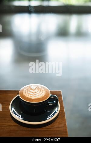 Porträt- oder vertikale Aufnahme einer Tasse Kaffee mit herzförmiger Latte Art auf einem Holztisch mit Bokeh-Hintergrund Stockfoto