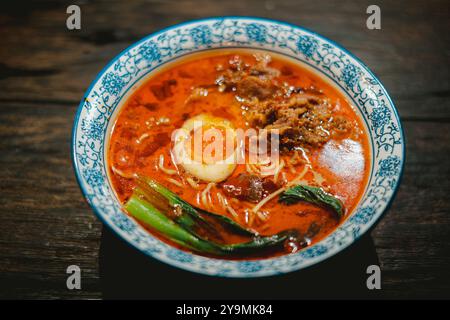 Eine Schüssel chinesische Nudelsuppe mit geriebenem Rindfleisch, einem hart gekochten Ei und einem Gemüse in einer blau-weiß gemusterten Keramikschale auf einem wo Stockfoto