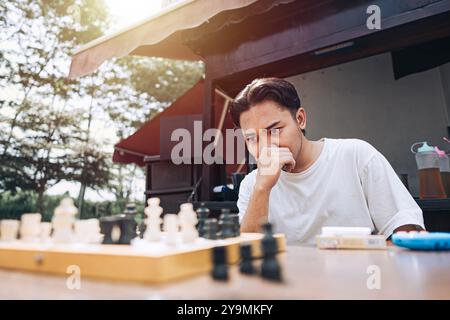 Ein südostasiatischer Mann ist verwirrt, während er nachmittags in einem traditionellen Café Schach spielt Stockfoto