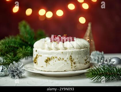 Ein wunderbarer Weihnachtskuchen mit Mascarponecreme und frischen Himbeeren auf einem dekorierten Feiertagstisch mit Tannenzweig und Dekorationen und Weihnachtsbeleuchtung Stockfoto