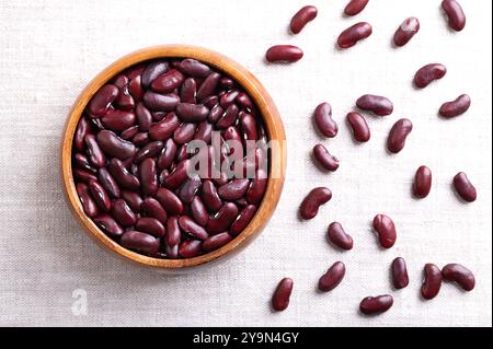 Getrocknete Kidneybohnen in einer Holzschale auf Leinengewebe. Rohe, ungekochte gewöhnliche Kidneybohnen, eine Sorte der gewöhnlichen Bohnen Phaseolus vulgaris. Stockfoto