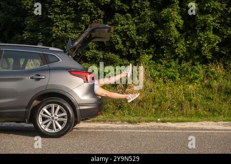 Humorvolle Szene von Beinen, die aus dem SUV-Trunk ragen Stockfoto