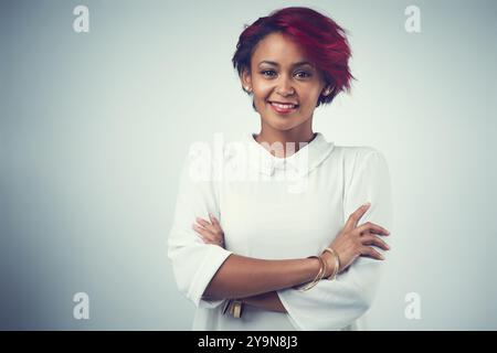 Afrikanische Frau, Porträt- und Haarpflege im Studio für Selbstvertrauen, Textur und Kosmetik mit roter Färbung. Weibliche Person, glücklich und gekreuzte Arme auf Grau Stockfoto