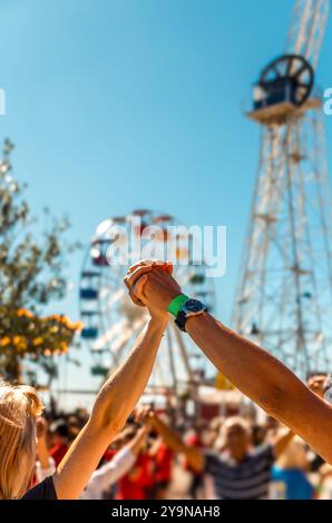 Zwei Personen mit erhobenen Armen und Händen tanzen den traditionellen katalanischen Tanz Sardana, während mehr Leute einen Refrain mit einem Riesenrad und Attra machen Stockfoto