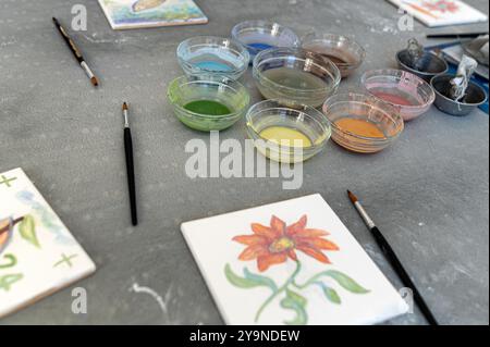 Kunstbedarf und bemalte Blumen auf einem Arbeitsplatz mit verschiedenen Aquarellfarben Stockfoto