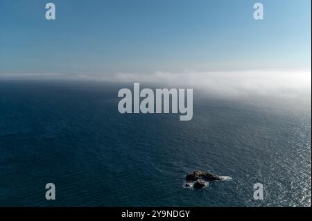 Ein Segelboot gleitet im Morgennebel über das ruhige Meer nahe einer felsigen Küste. Stockfoto