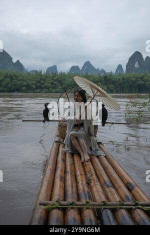 Hanfu-Mädchen mit Schirm auf Bambusfloß in Xingping posiert mit Kormoranen Stockfoto