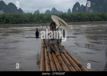 Hanfu Girl sitzt auf einem Bambusfloß und hält einen Regenschirm, während sie ihre Haare fixiert Stockfoto