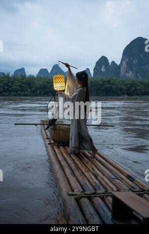 Hanfu-Mädchen, das eine Laterne auf einem Bambusfloß hält, Xingping, China. Vertikal Stockfoto