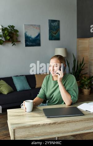 Eine fröhliche junge Frau in Übergröße plaudert am Telefon, während sie Kaffee in ihrem Wohnzimmer schlürft. Stockfoto
