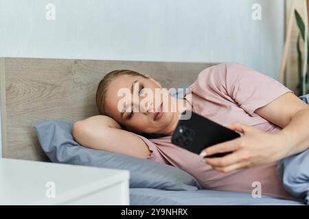 Eine junge, schöne Frau in Übergröße liegt bequem auf ihrem Bett, in ihrem Handy eingesogen. Stockfoto